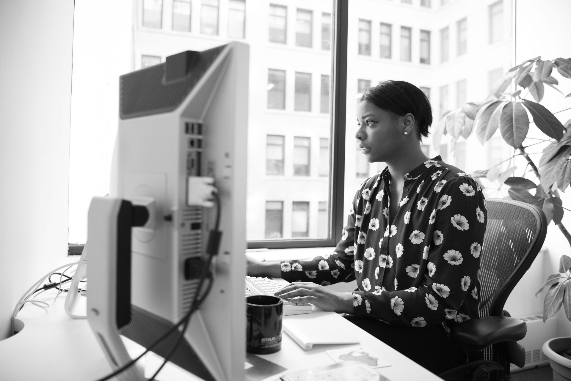 Person typing at a desk in front of a large monitor in a bright office.