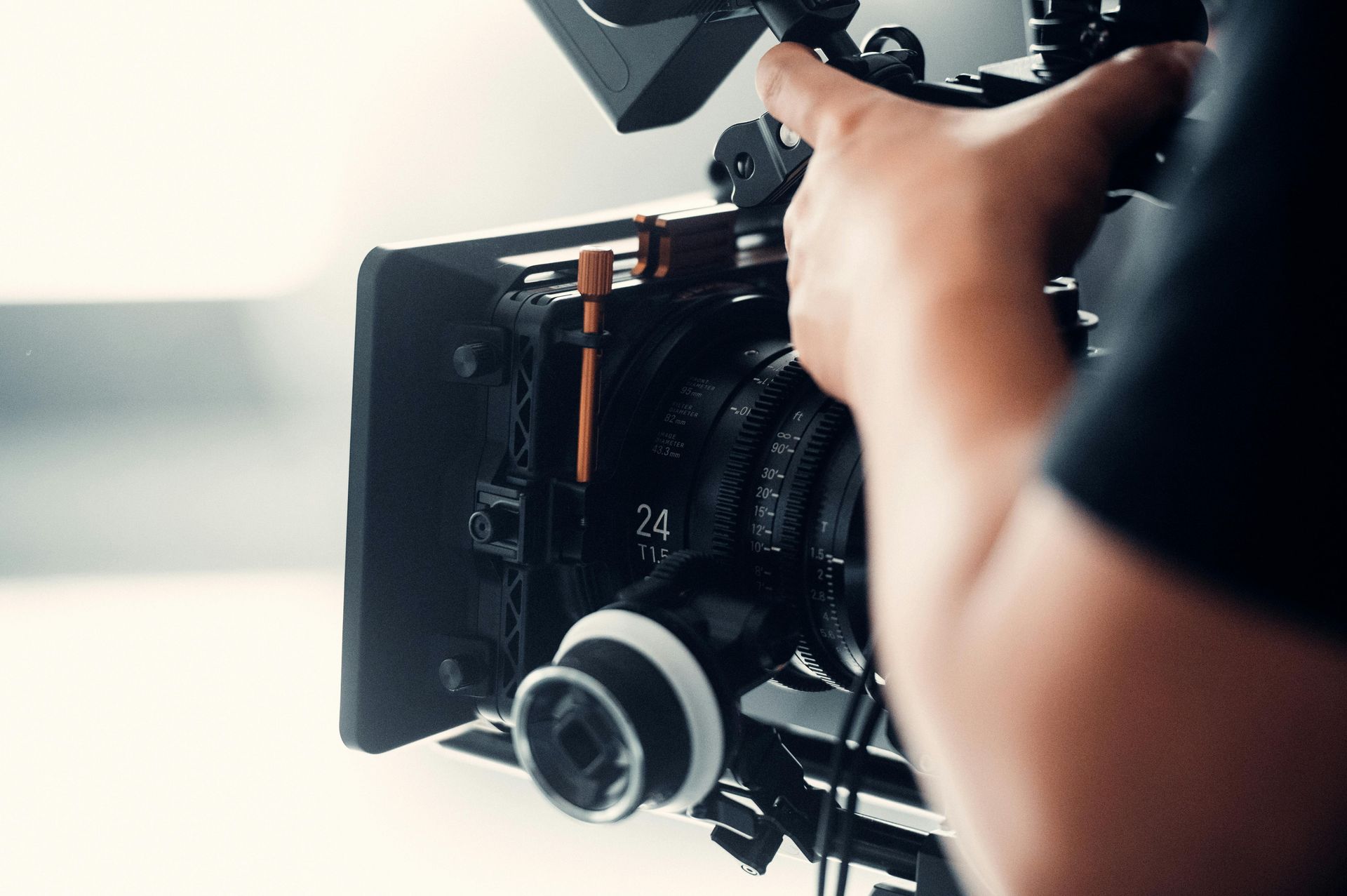 Person operating a professional video camera with a matte box and lens, close-up view