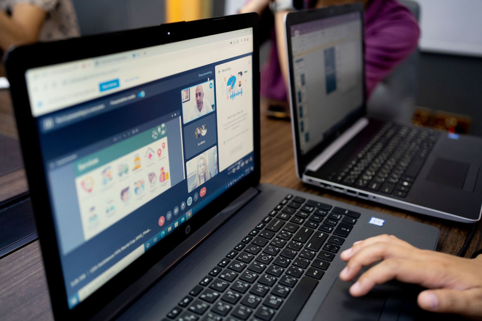 Two laptops on a desk showing a website, with a hand using the front keyboard