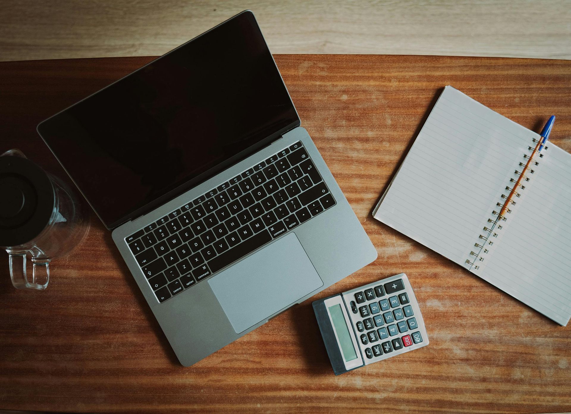 A laptop computer is sitting on a wooden desk next to a notebook and a calculator.
