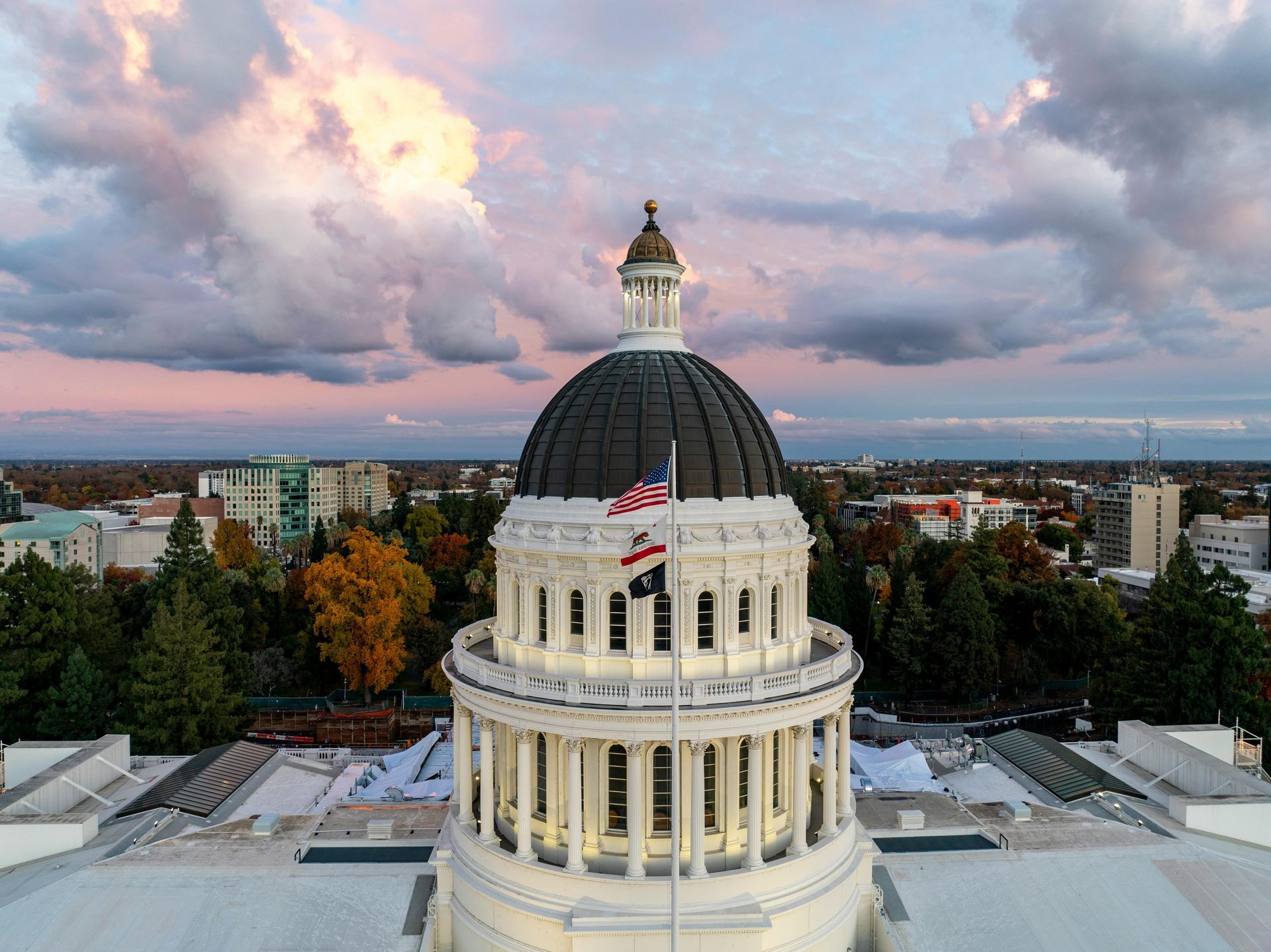 A high-angle view of the California State Capitol dome at sunset with the American and state flags flying.