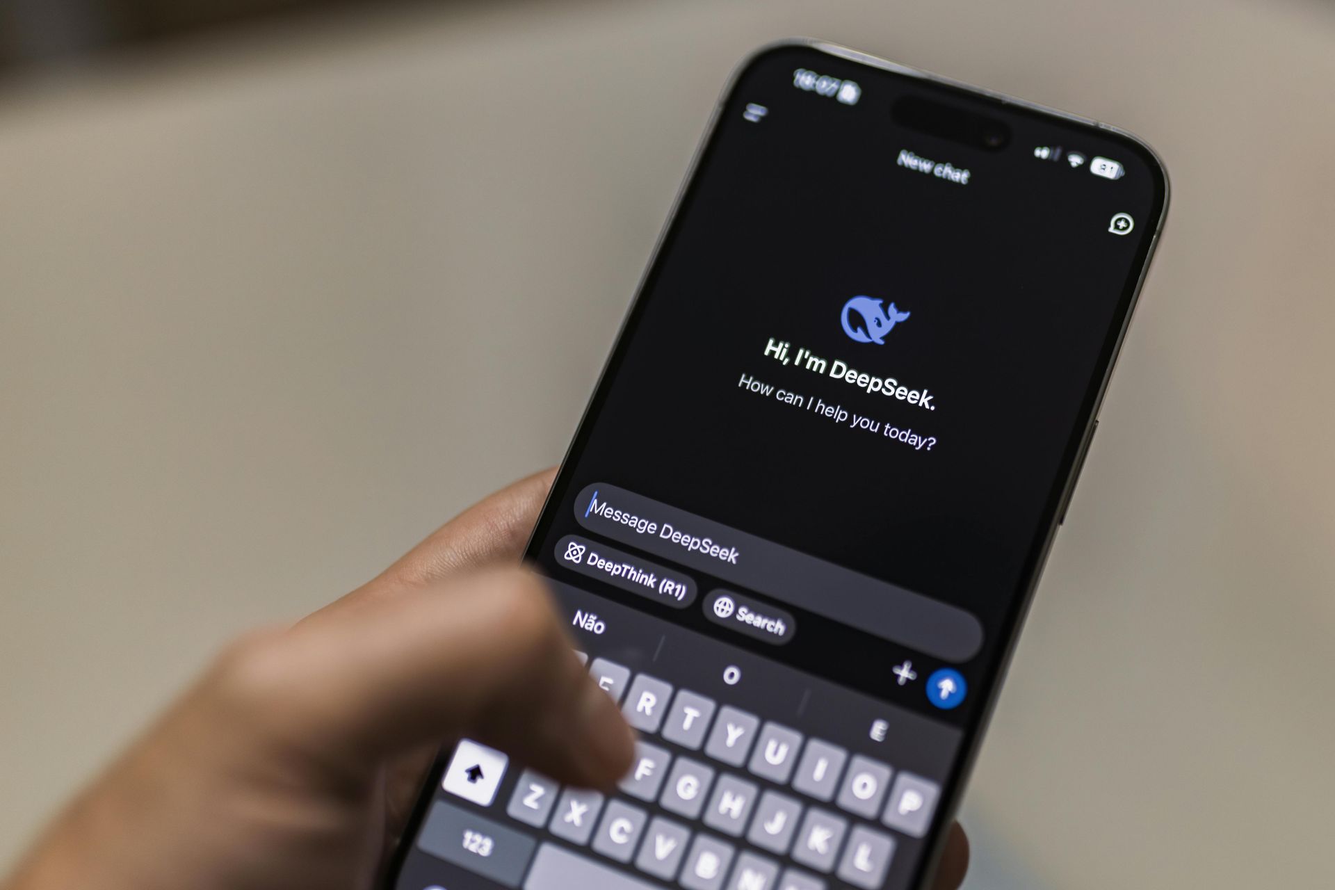 A person holds a smartphone displaying the DeepSeek AI chatbot interface on a dark screen, with a keyboard active.