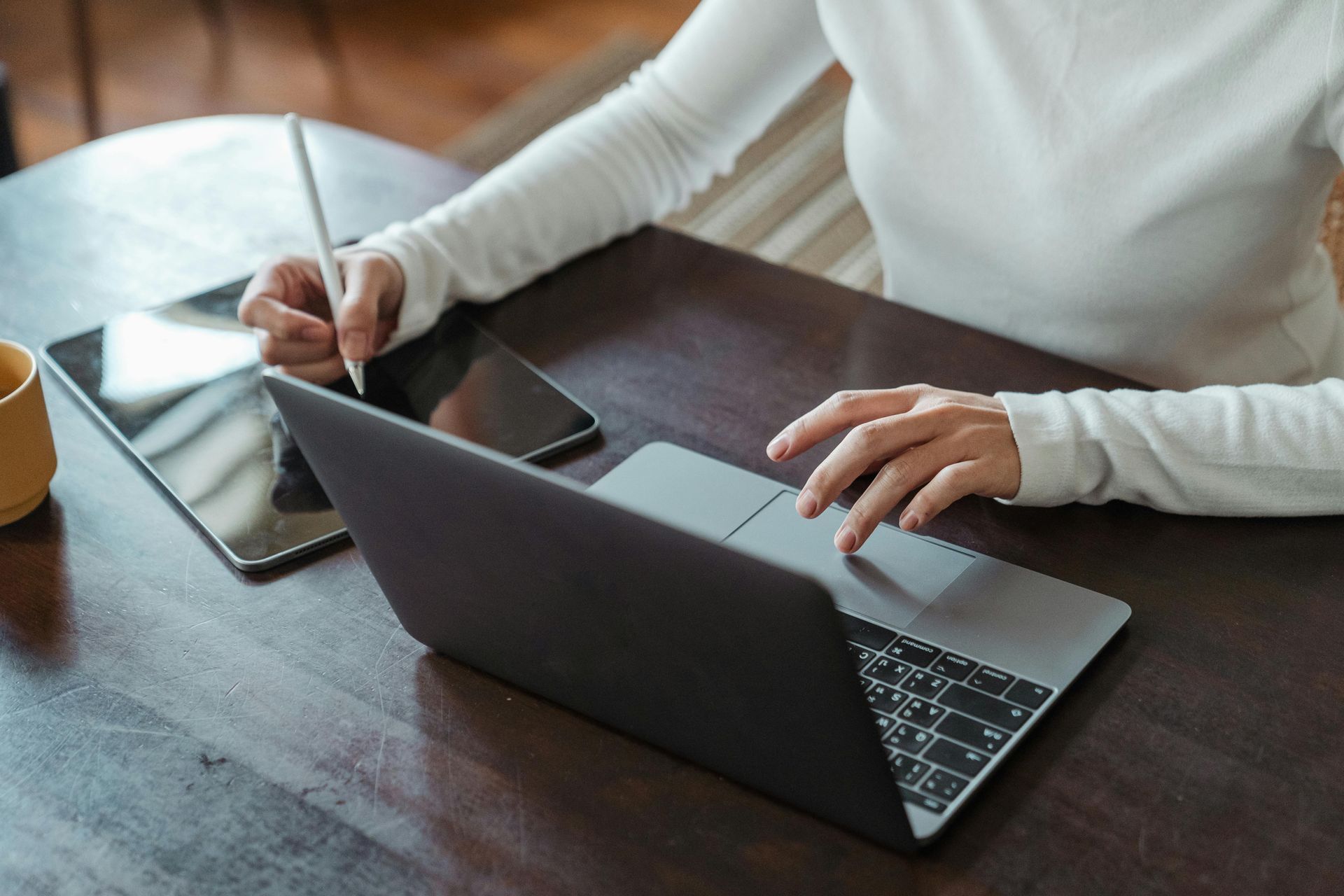 A desk with a lamp, a pencil holder, a white mug, and a laptop in front of an office chair against a plain wall.