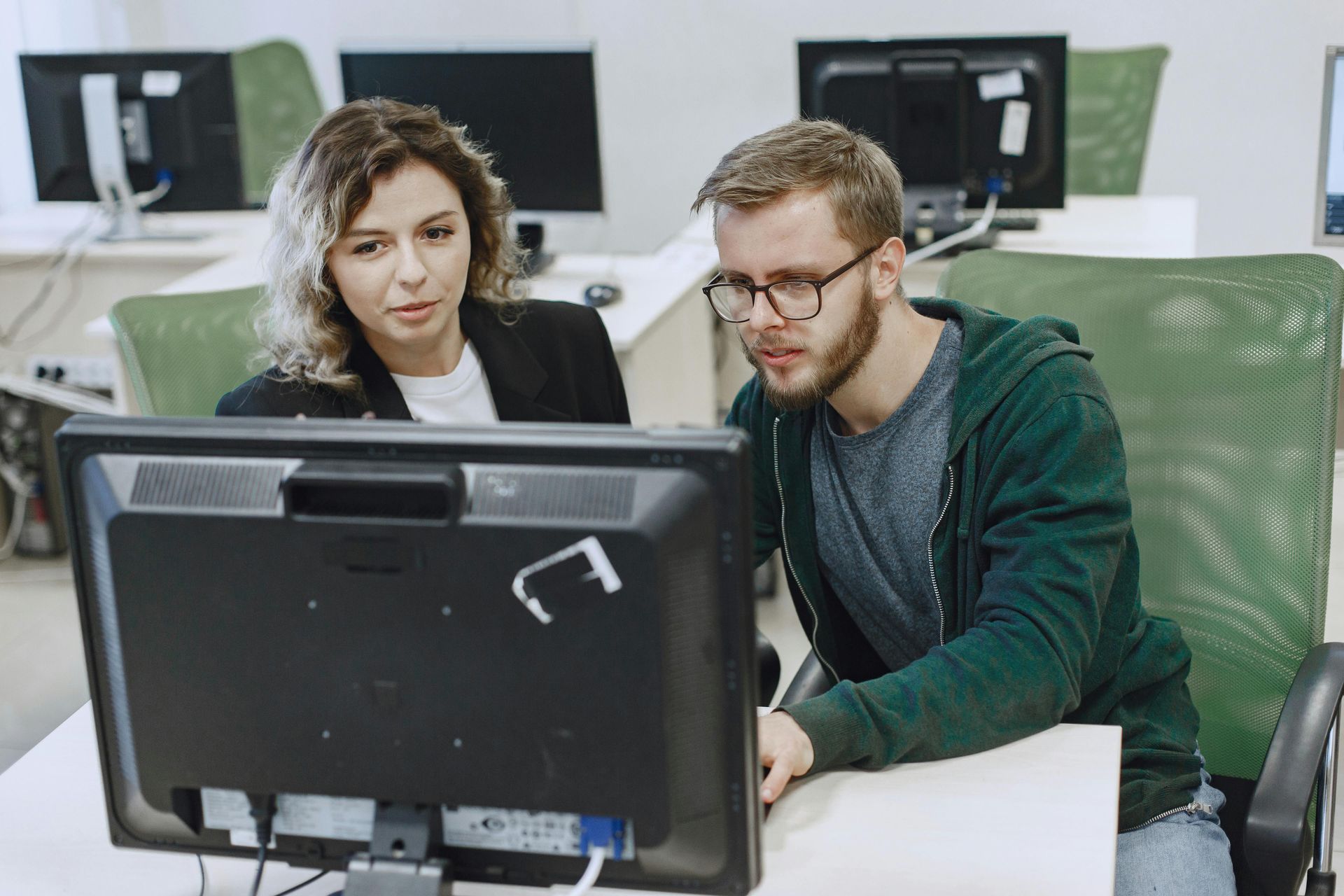 Two people sitting at a desk in an office, collaborating while looking at a computer monitor.