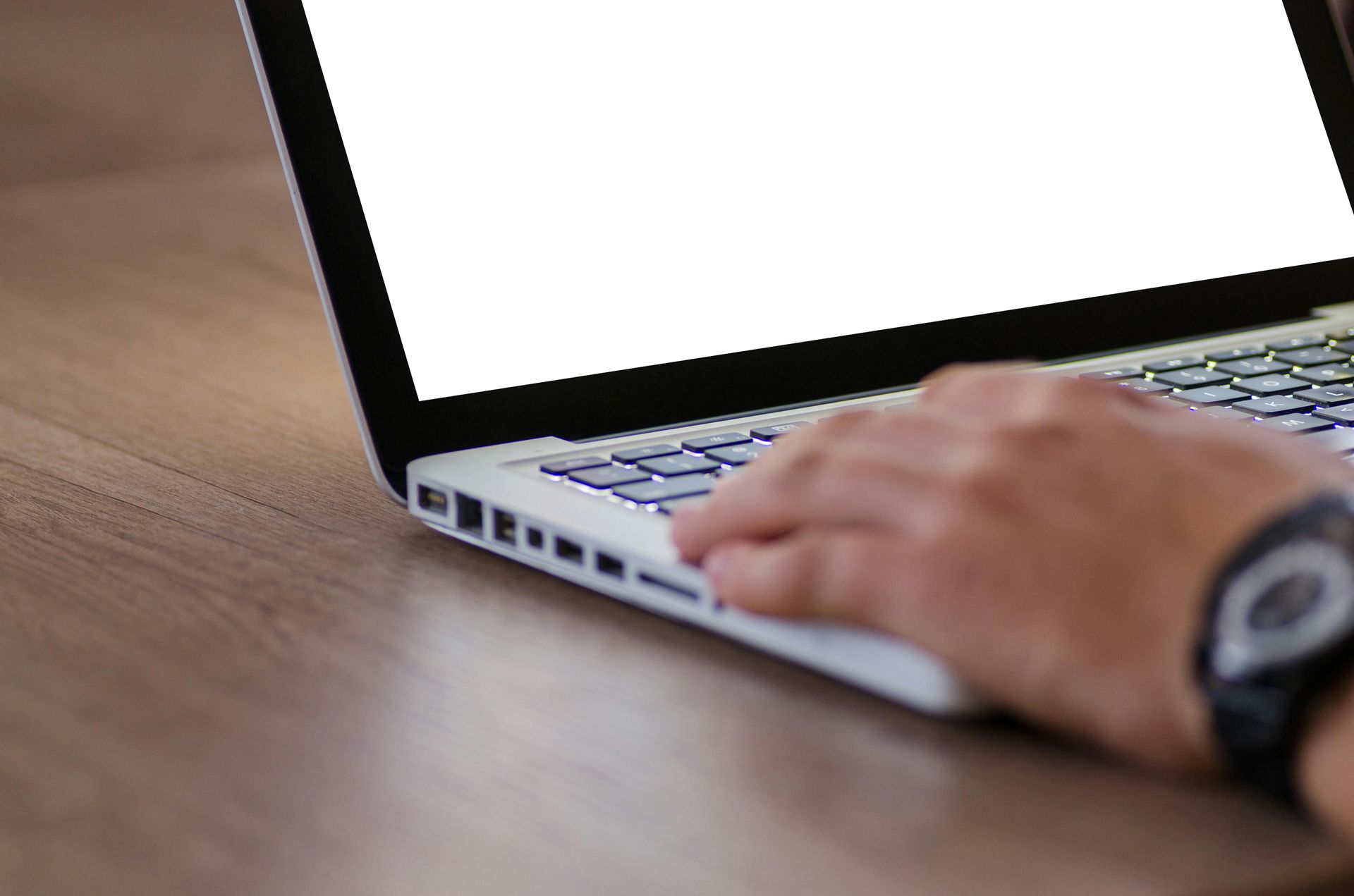 A person's hand resting on the keyboard of a laptop with a blank white screen, set on a wooden desk.