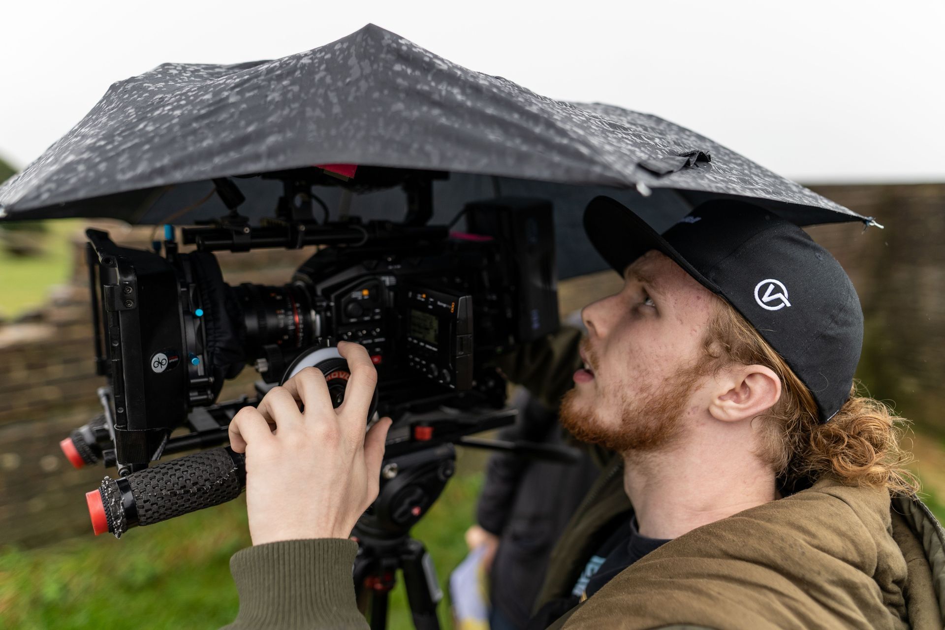 Cameraman under a rain cover adjusting a professional video camera outdoors