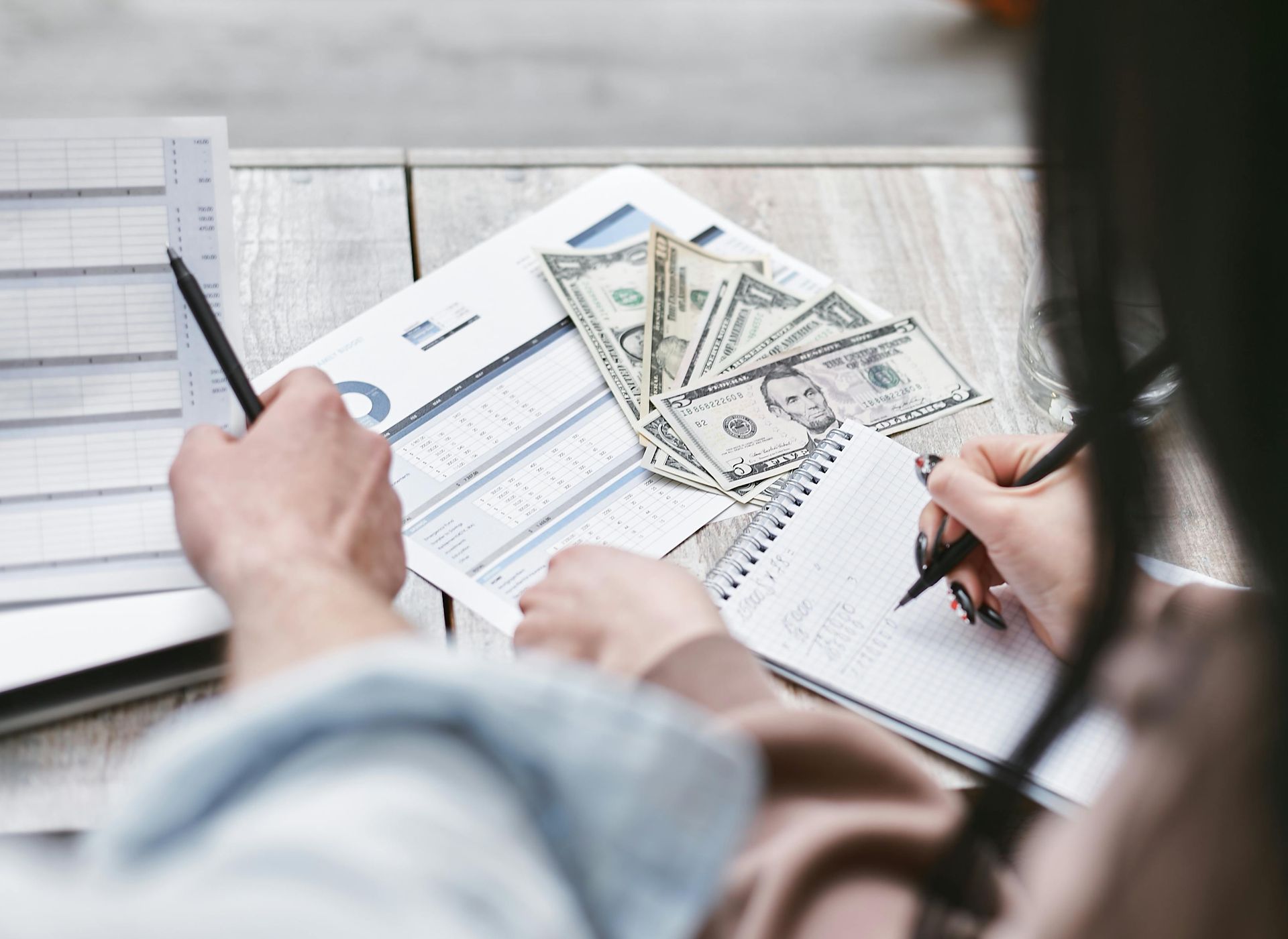 A woman is writing in a notebook next to a pile of money.