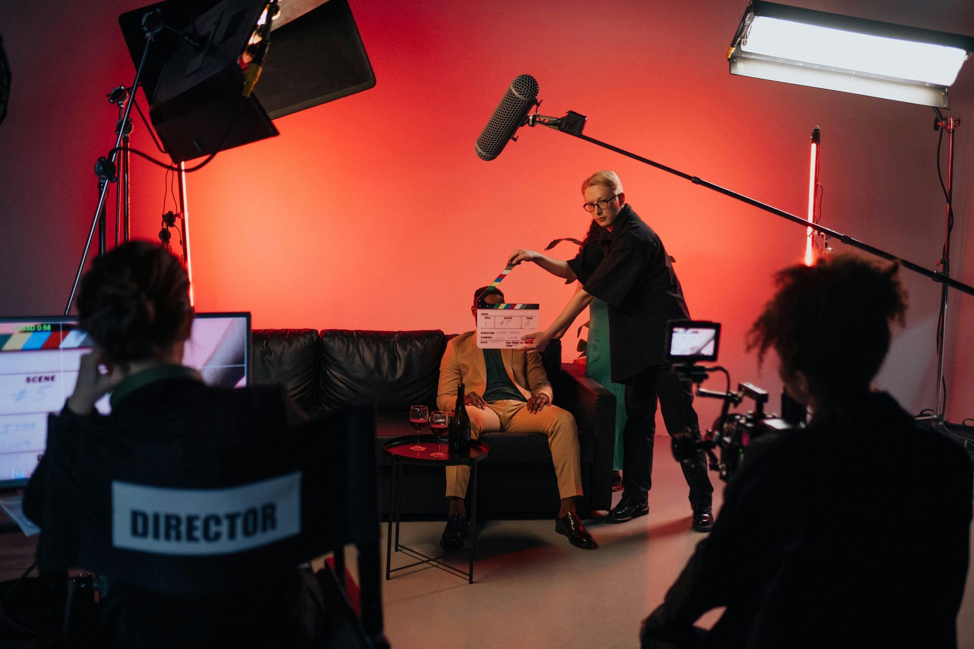 Film crew recording an interview in a red-lit studio, with camera, boom mic, and director chair visible