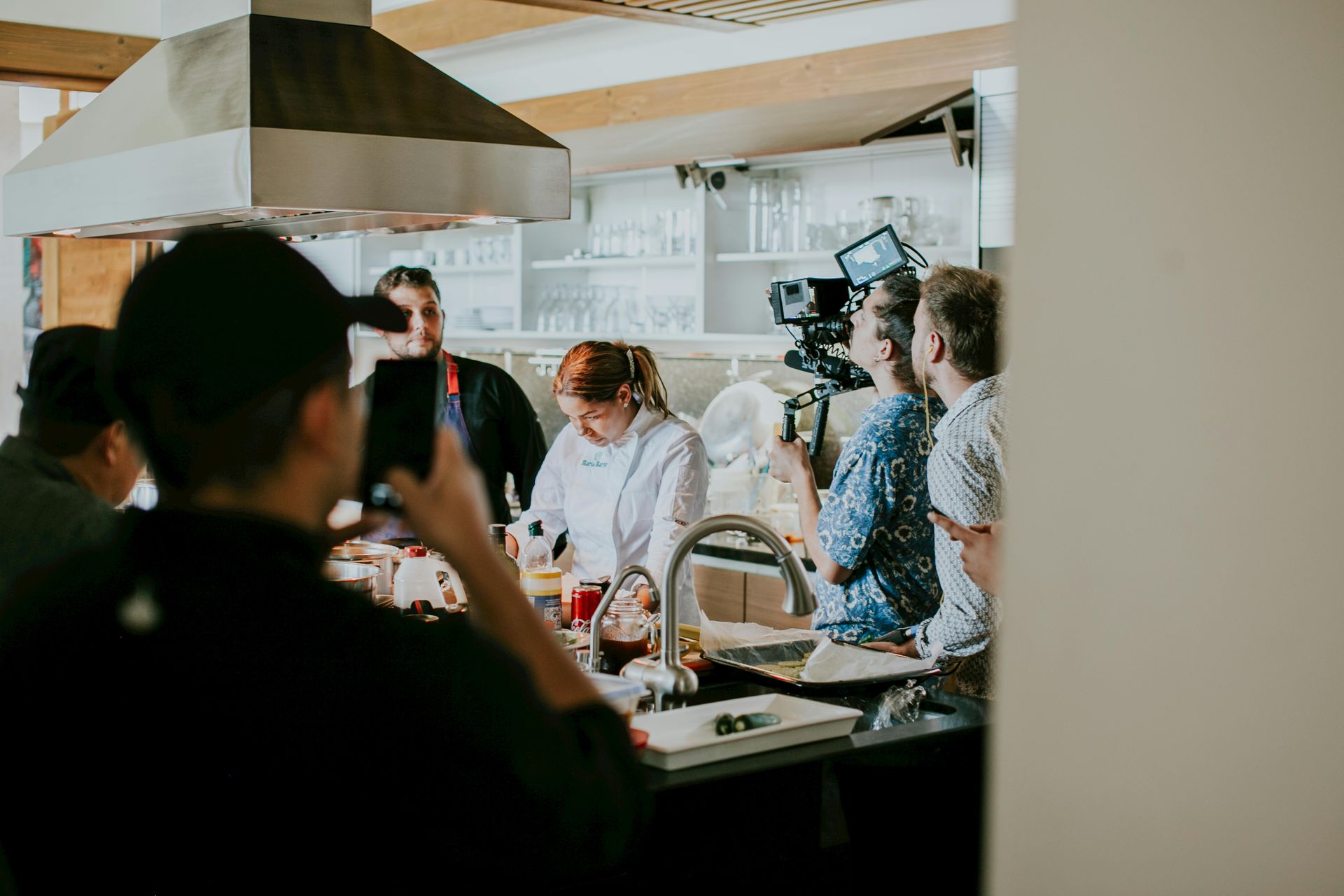 A video production crew films a chef preparing food in a brightly lit, modern kitchen.