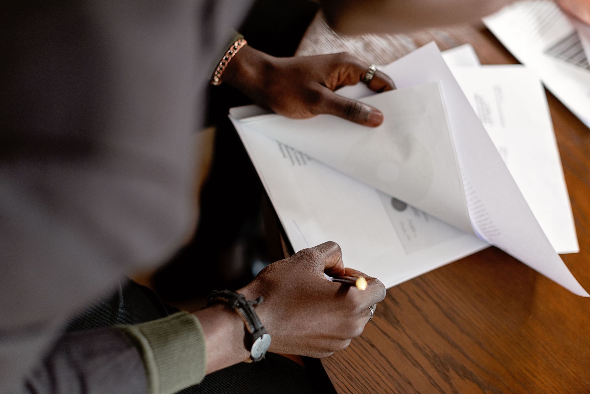 Hands opening white paper documents on a wooden table