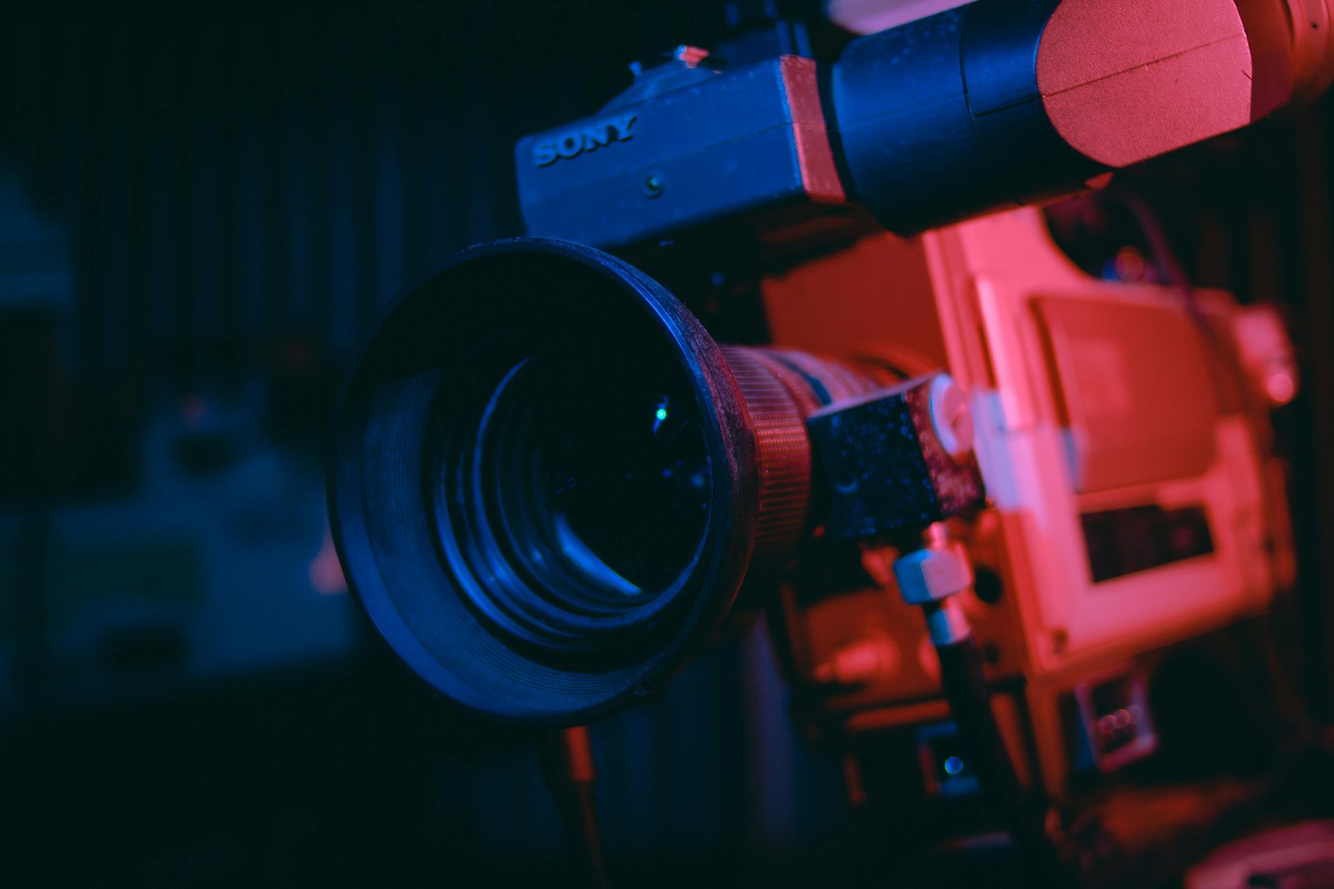 A close-up shot of a Sony professional video camera under dramatic blue and red studio lighting.