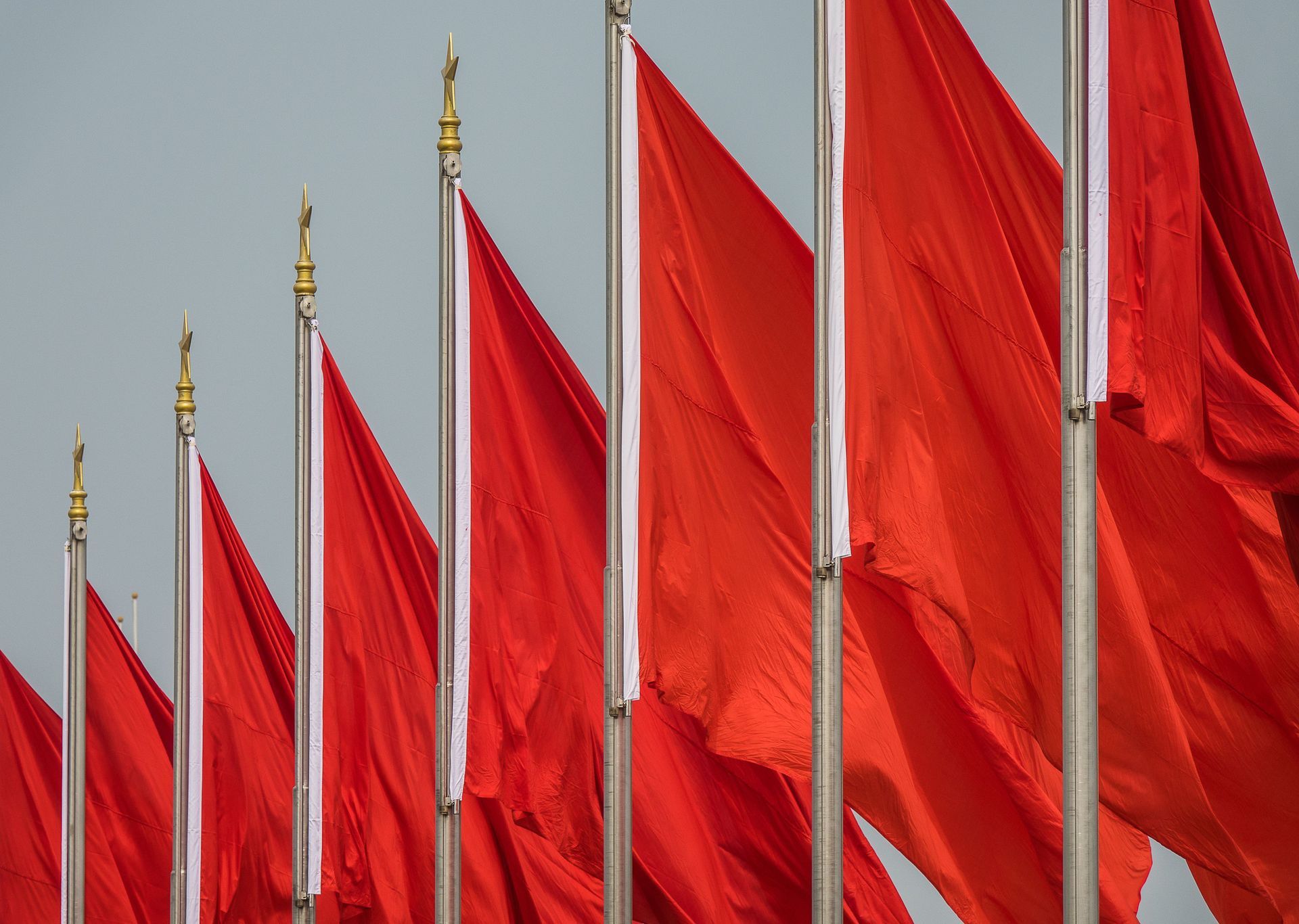 Row of bright red flags on silver poles against a gray sky