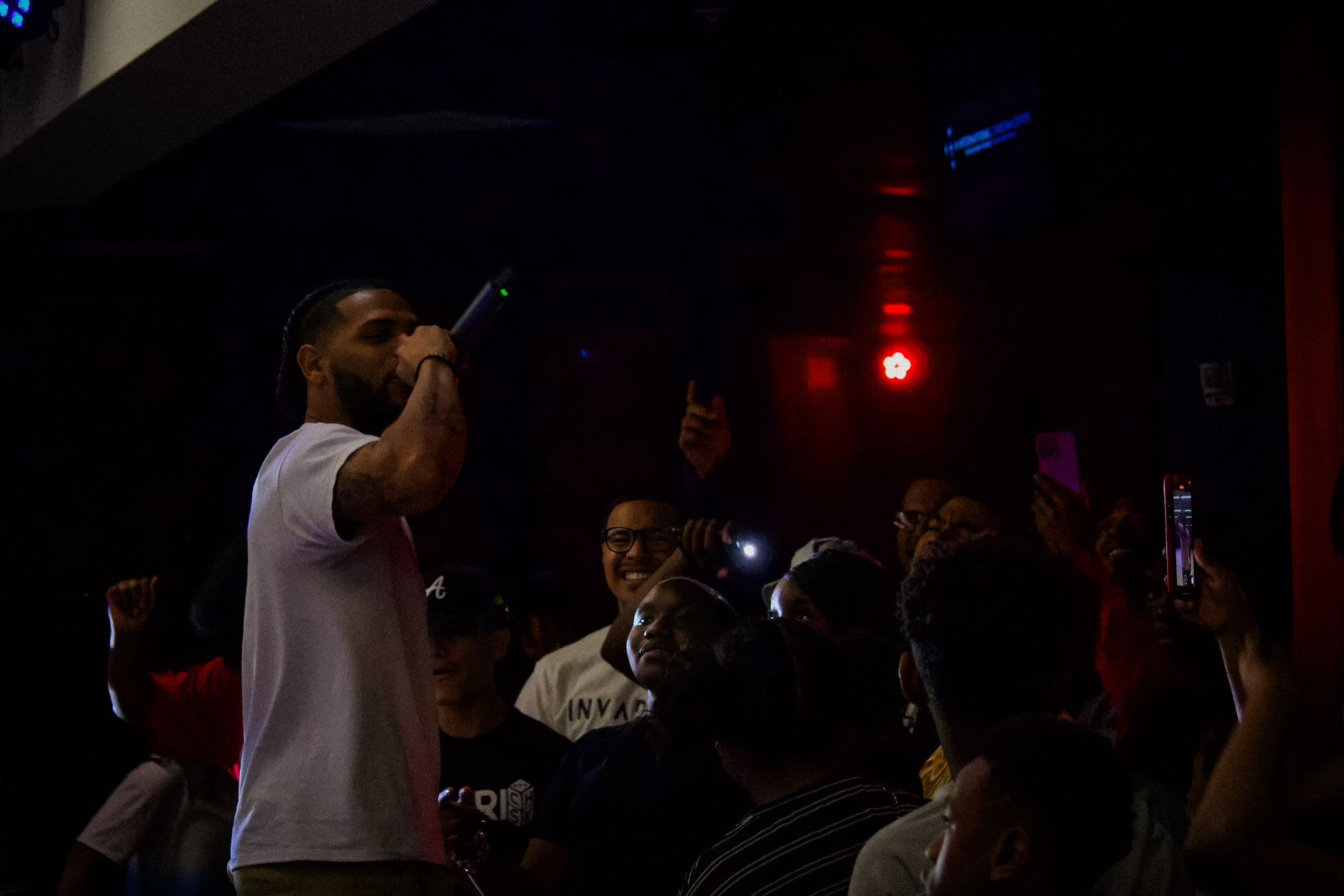 Man performing with a microphone in a dark venue; crowd watches, some with phones raised.