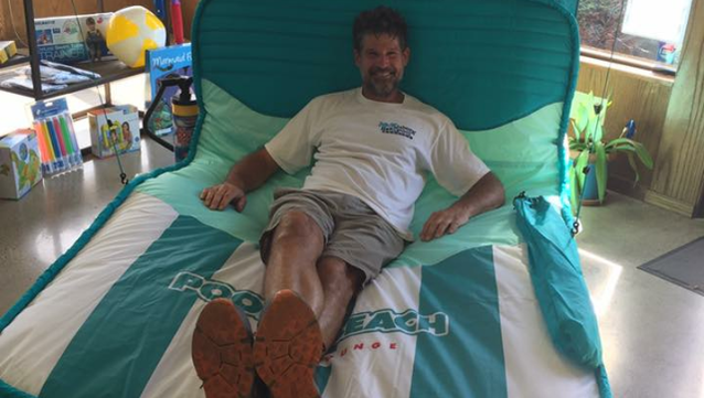 Person reclining on a teal-and-white lounger in a bright room, smiling with legs extended.