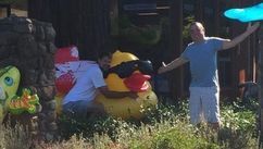 Two people standing beside a giant yellow duck statue outdoors, one holding a blue umbrella