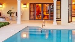 Covered patio with a swimming pool, white columns, and warm lit glass doors at dusk