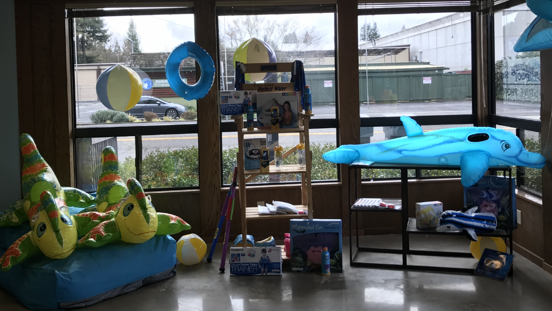 Indoor play area with blue and green inflatable toys, shelves, and large windows looking outside