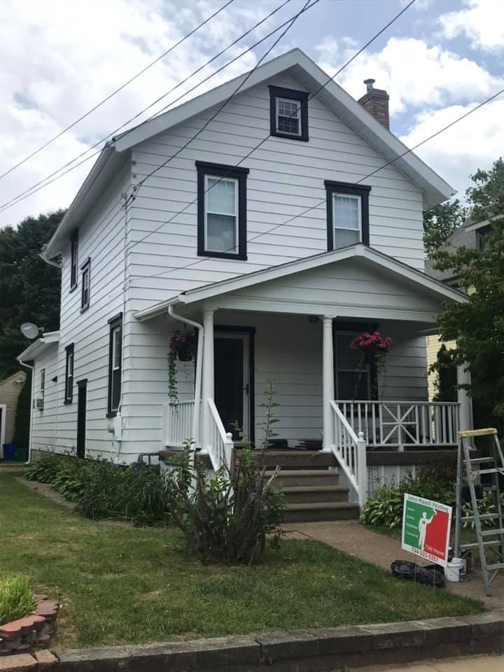 White two-story house with black window frames, small porch, and green lawn.