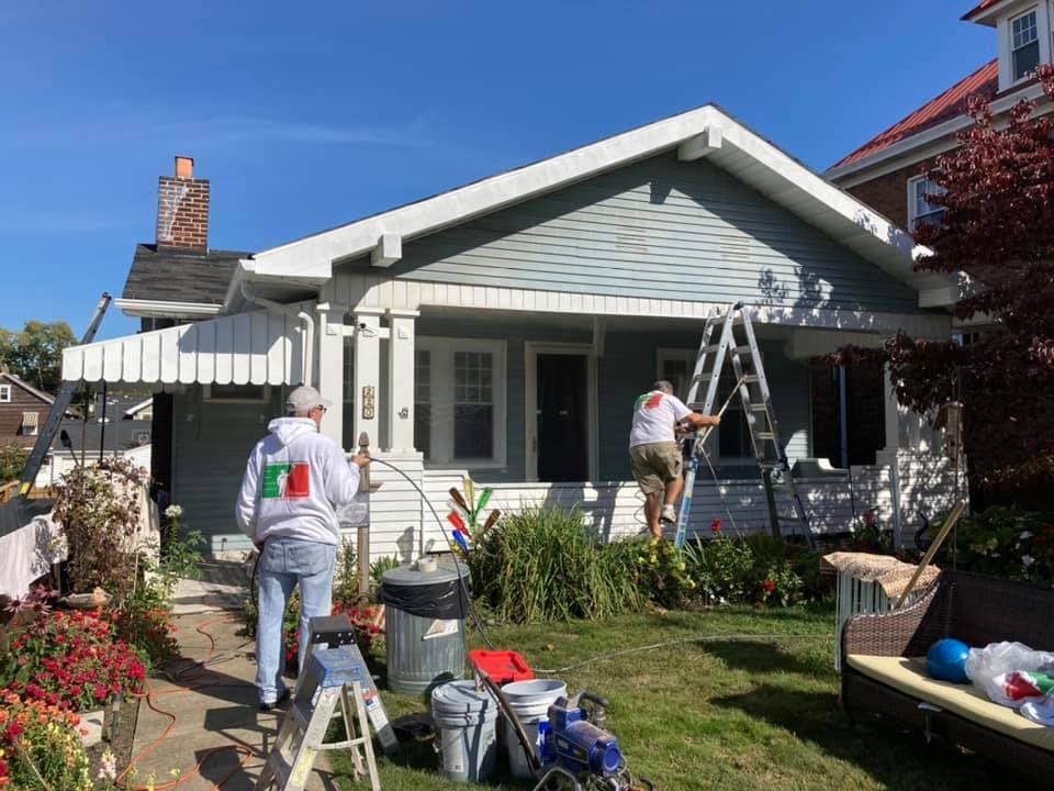 People painting a light blue house on a sunny day.