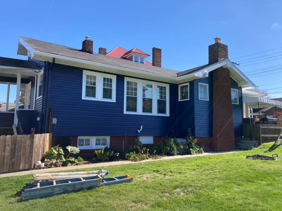 Blue house with white trim, red chimney on a sunny day. Green lawn, ladder.