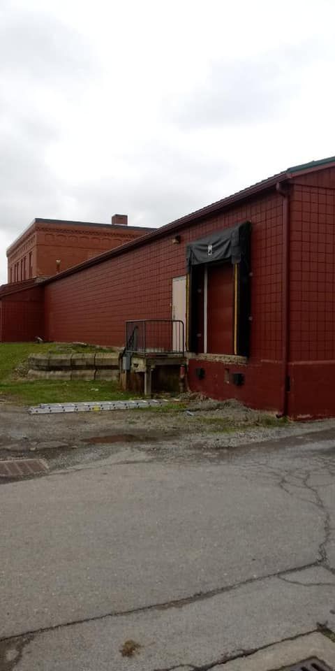 Red brick building with loading dock, gray pavement in foreground. Overcast sky.