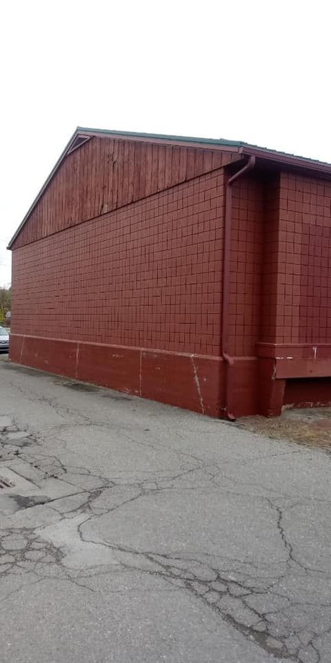 Red brick building with wooden roof next to cracked asphalt.