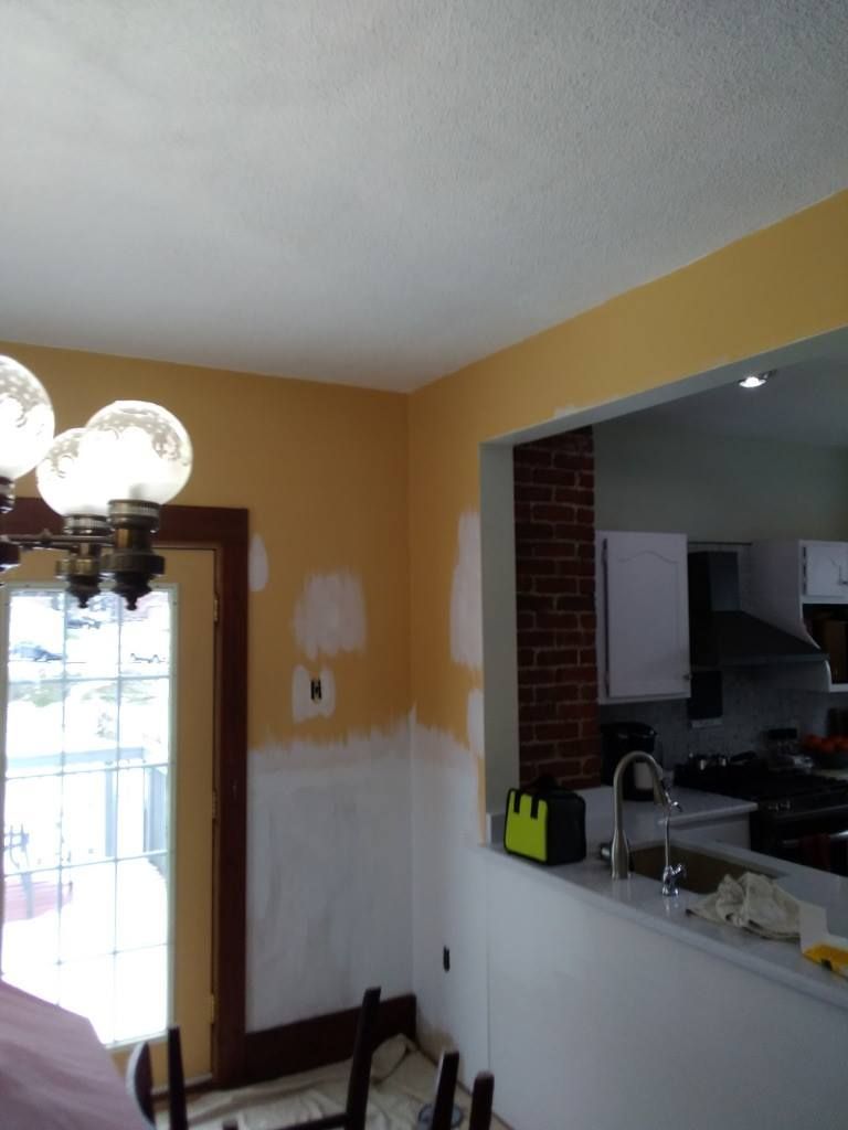 Kitchen interior, walls partially painted yellow and white; doorway, pass-through to kitchen with exposed brick, sink.