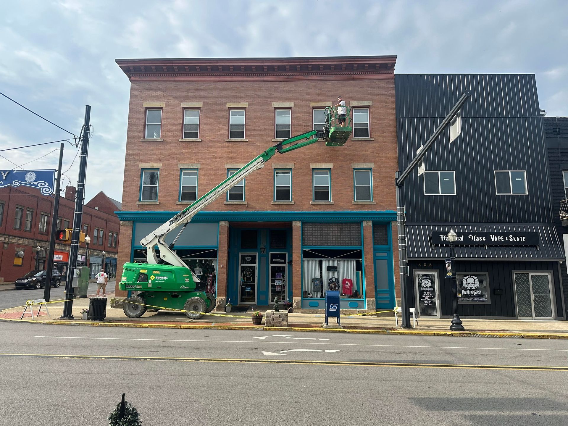 A cherry picker lift being used on a three-story brick building facade. Two adjacent storefronts.