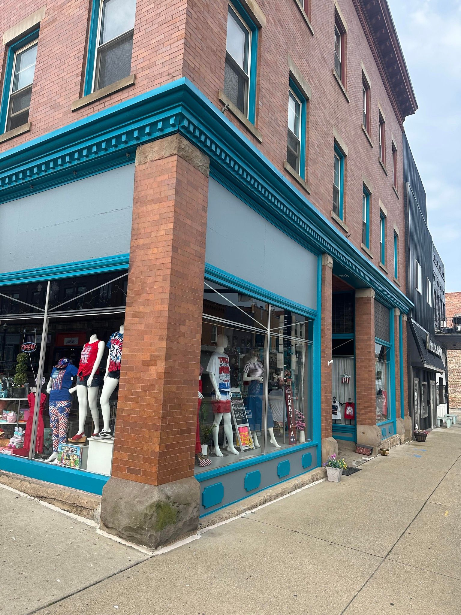 Brick building with teal trim and shop window displaying mannequins.