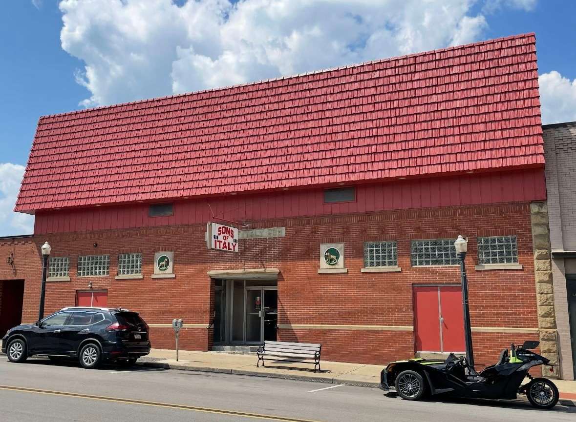 Red brick building with a red tiled roof, black car and motorcycle in front, blue sky.