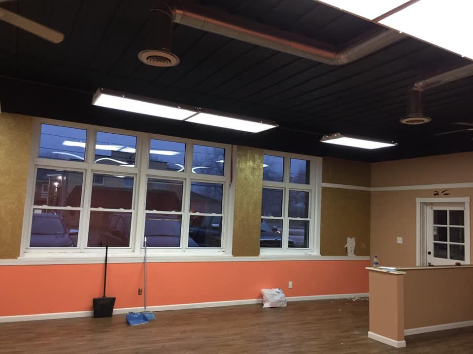 Interior of a room with large windows, an orange wall, and a black ceiling with fluorescent lights.
