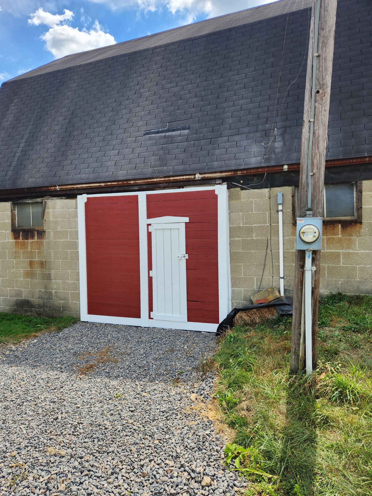 Red barn doors on a gray block building with a black roof, gravel driveway, and utility pole.