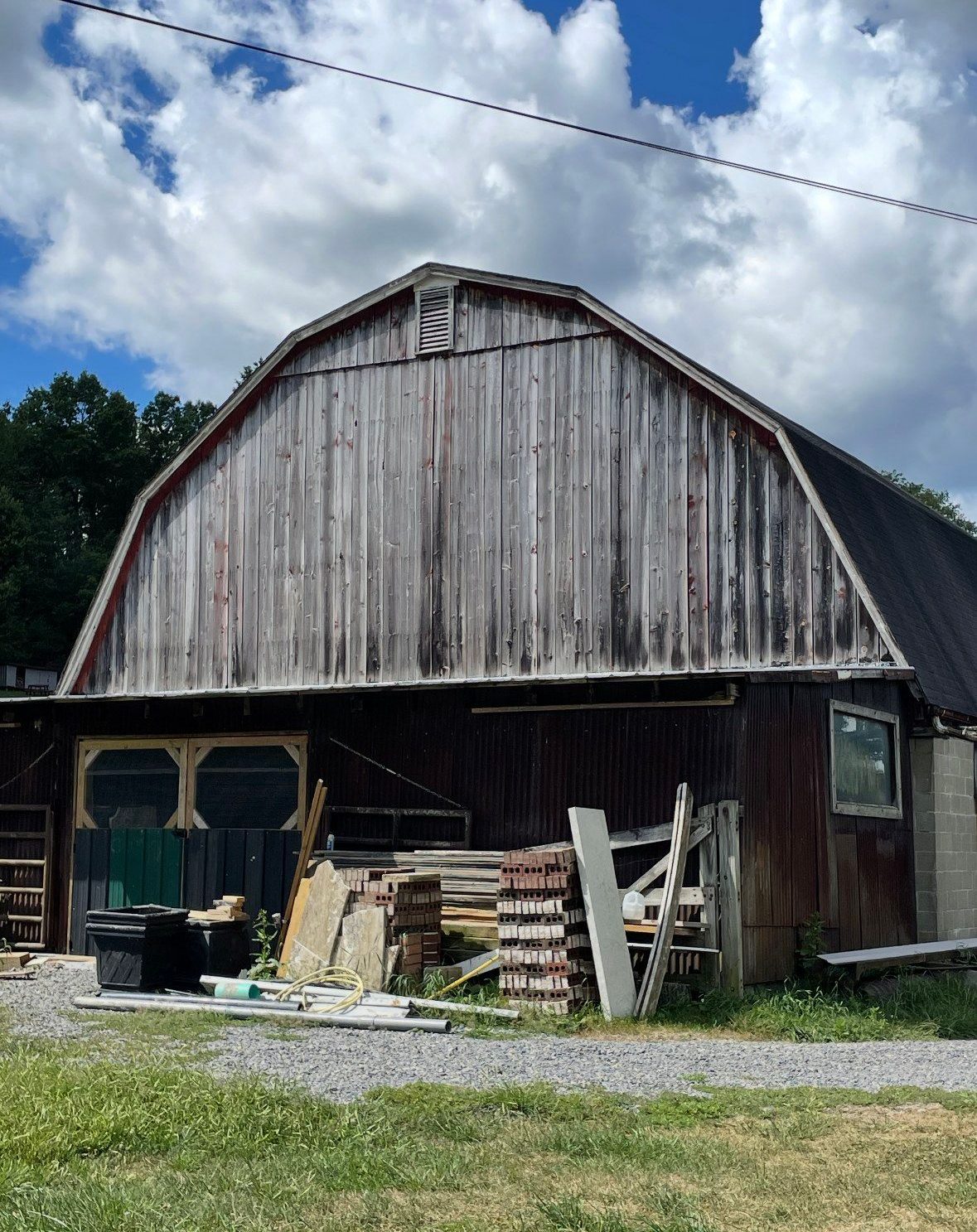 Weathered wooden barn on a gravel lot under a partly cloudy sky.