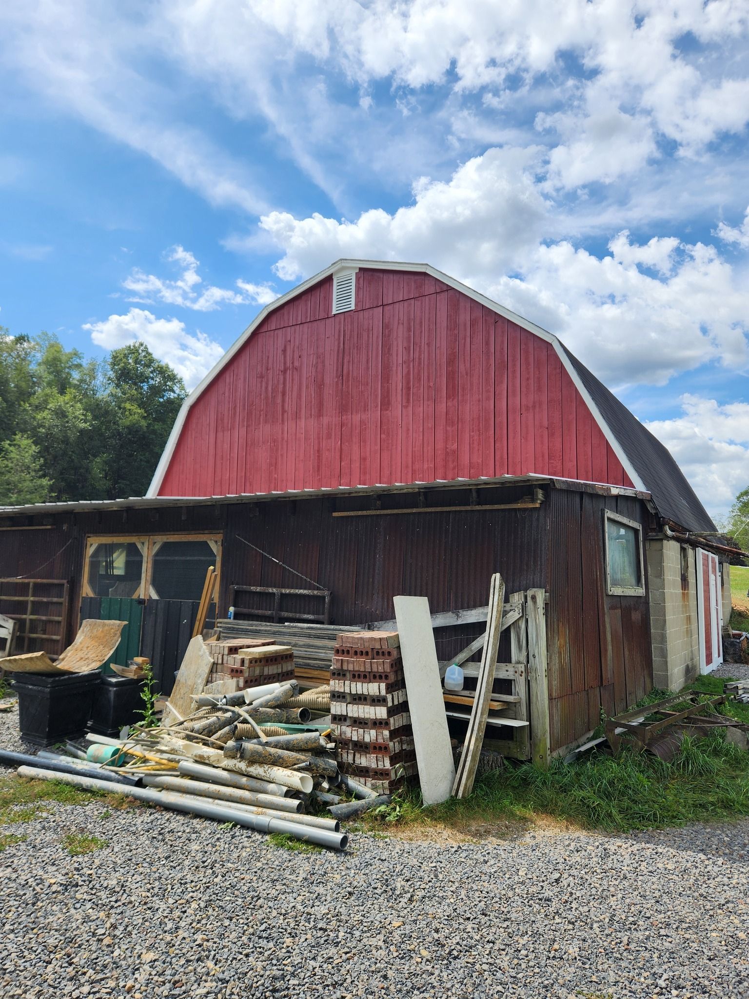 Red barn with a dark brown extension; outdoor setting with blue sky and clouds.