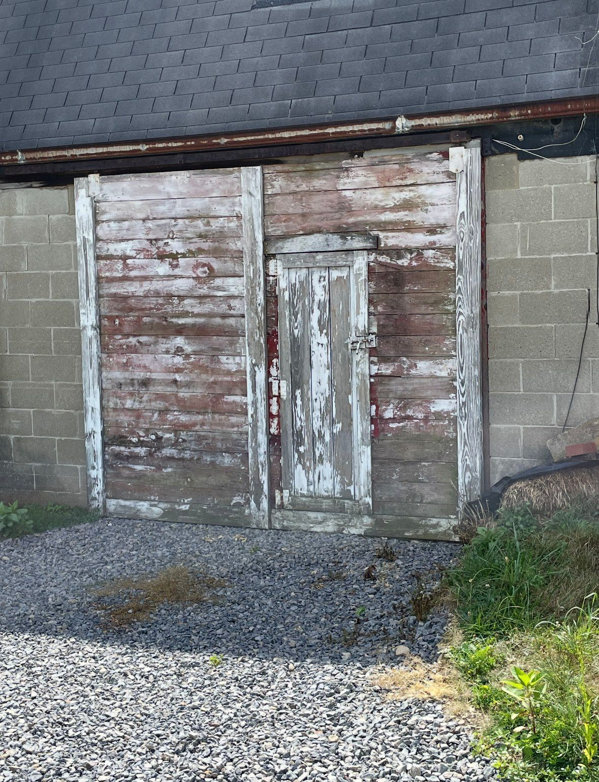 Weathered wooden doors on a gray cinder block building, surrounded by gravel and grass.