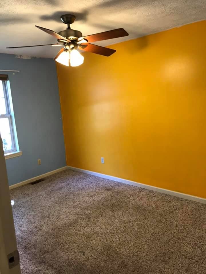 Bedroom with blue and yellow walls, ceiling fan, and brown carpet.