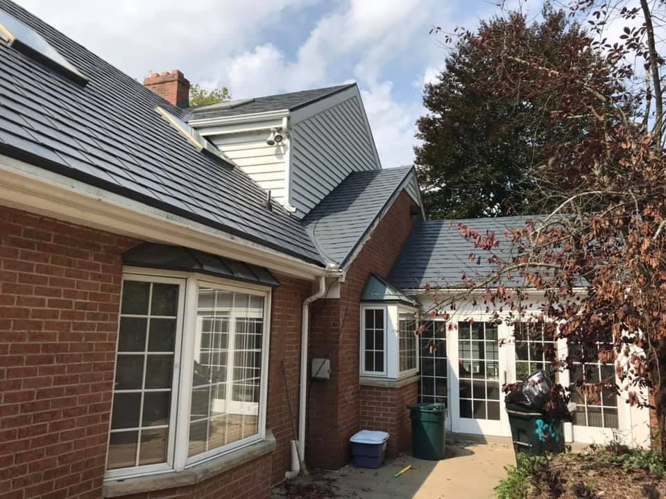 Brick house with dark gray roof, white windows, and a tree with fall foliage.
