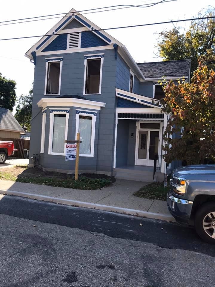 Blue-sided house with white trim and windows under a blue sky, ladder on the side.