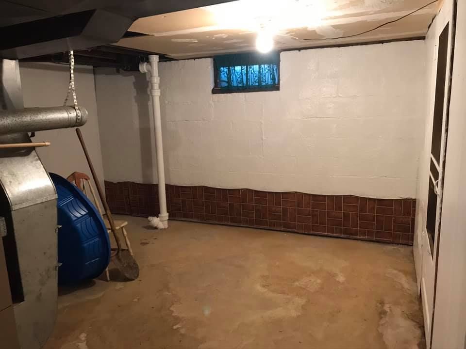 Basement interior with white walls, brown brick paneling, a small window, and a concrete floor.