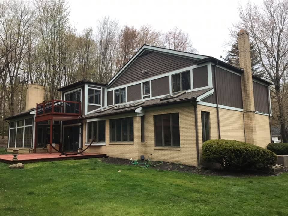 Two-story house with brown siding, a tan brick base, and a red deck overlooking a green lawn.