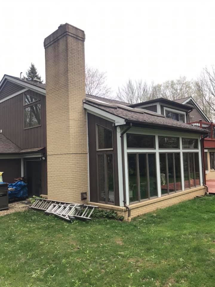 Exterior view of a brown house with a sunroom and a beige brick chimney on a green lawn.