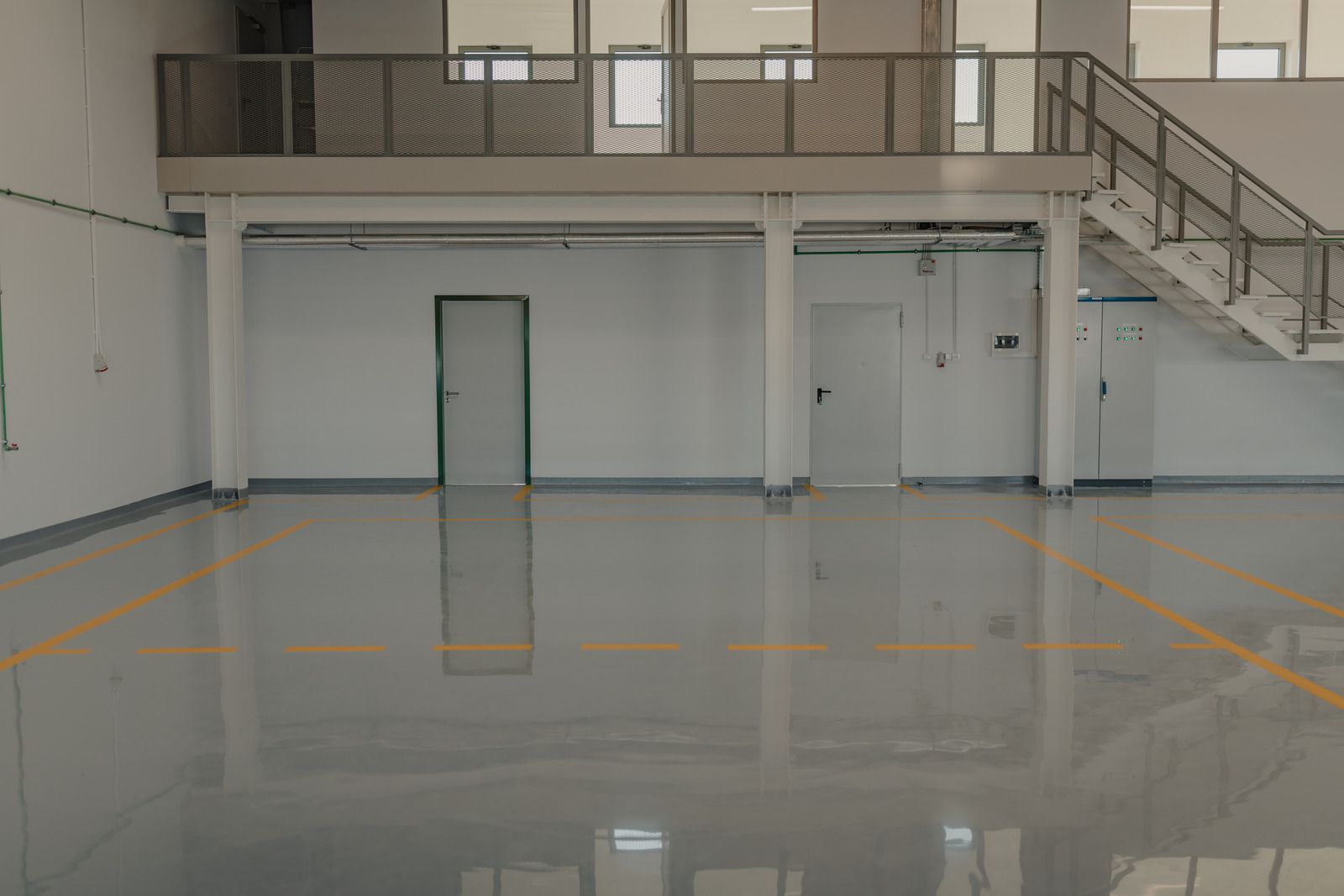 Empty, spacious, light-filled industrial interior with a raised platform, stairs, and shiny, reflective floor.