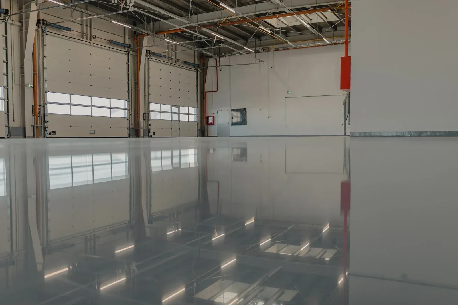 Shiny gray warehouse floor reflecting ceiling lights and closed bay doors.