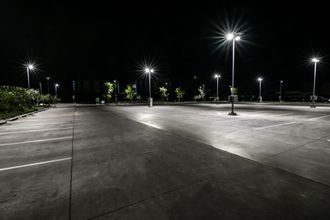 An empty parking lot is lit up at night with lots of street lights.