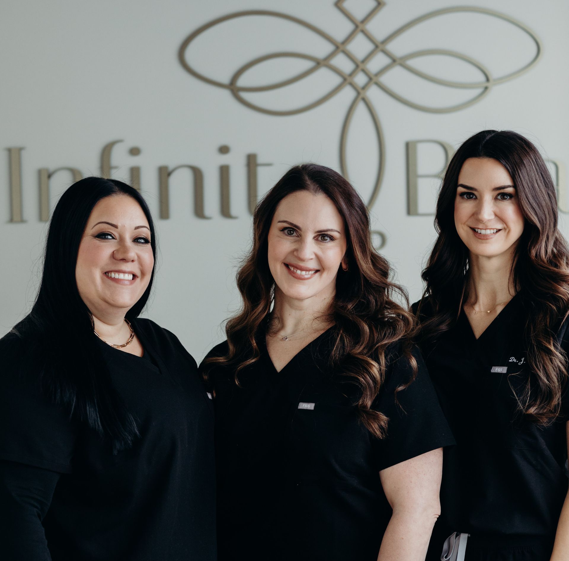 Three women in black tops smiling, in front of a sign that says 