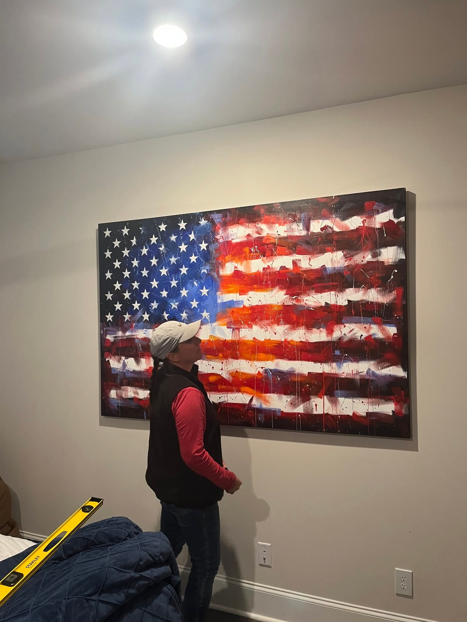 Person standing before a large American flag painting on a wall in a room.