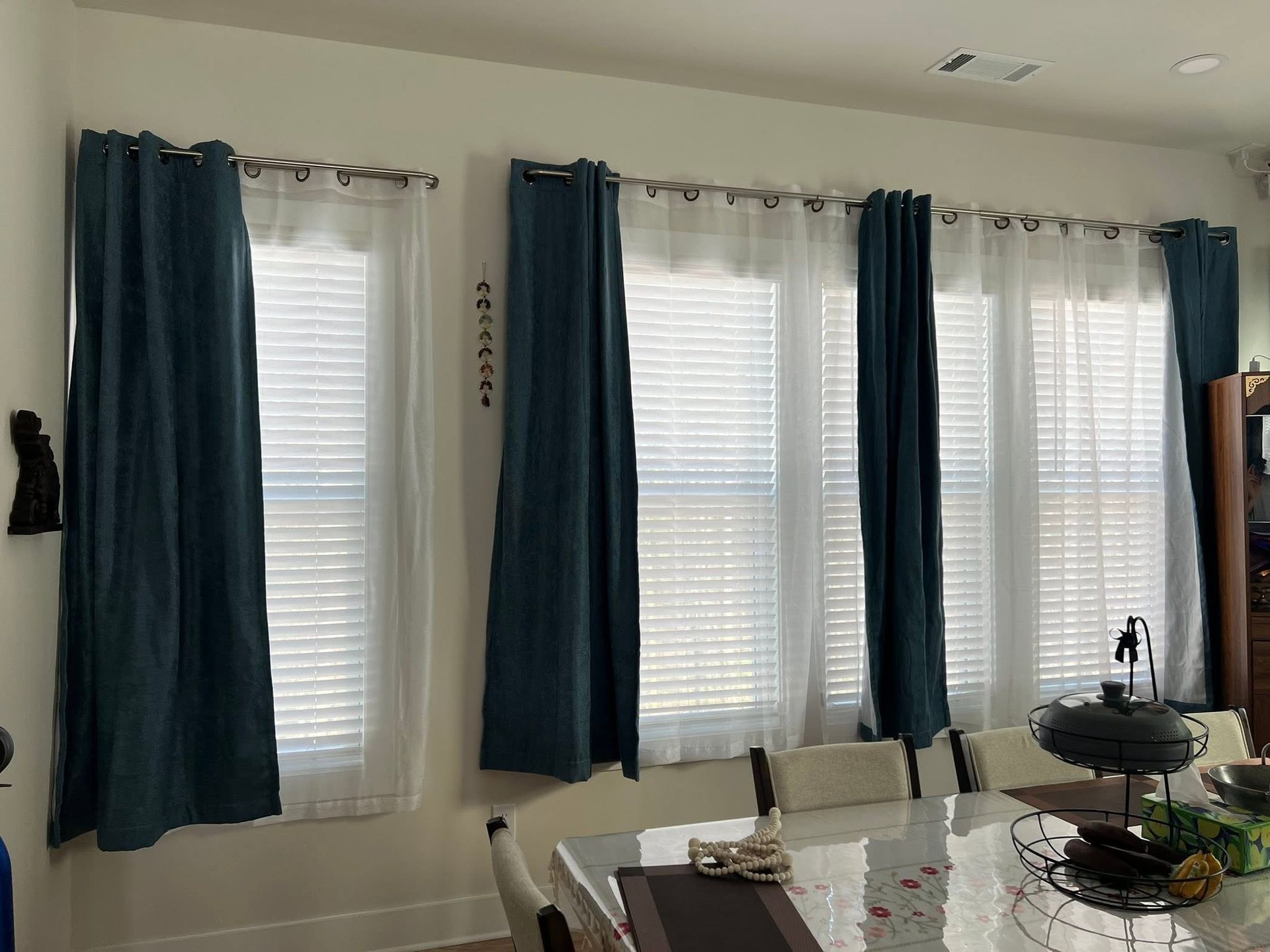 Living room windows with blue curtains and white blinds, beside a dining table and chair