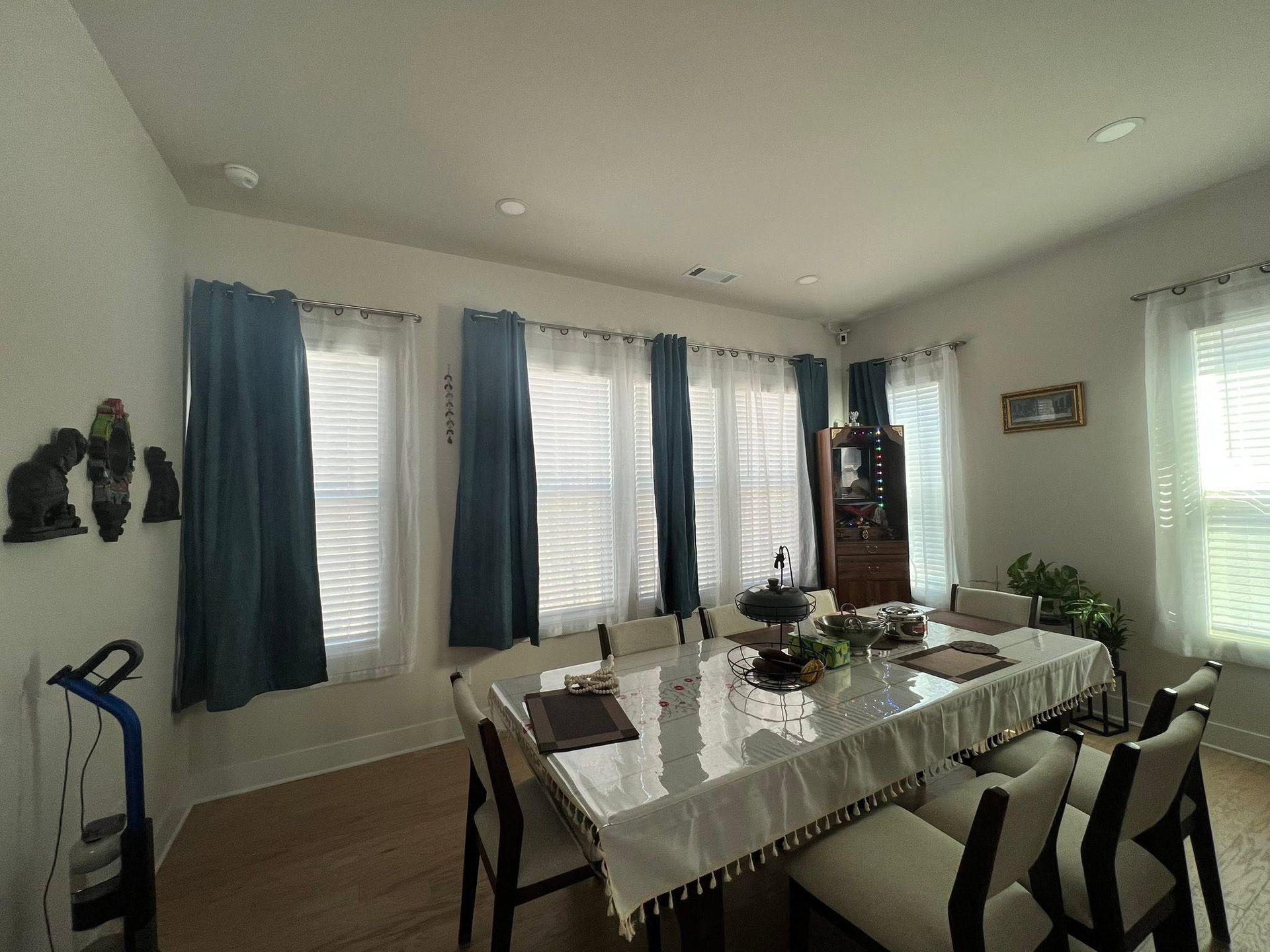 Dining room with large windows, blue curtains, and a table set with a white tablecloth and chairs.