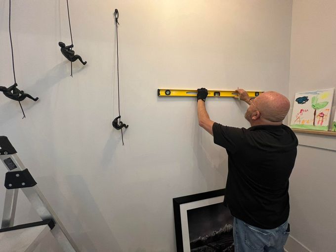 Person using a level to hang a frame on a white wall in a room under renovation