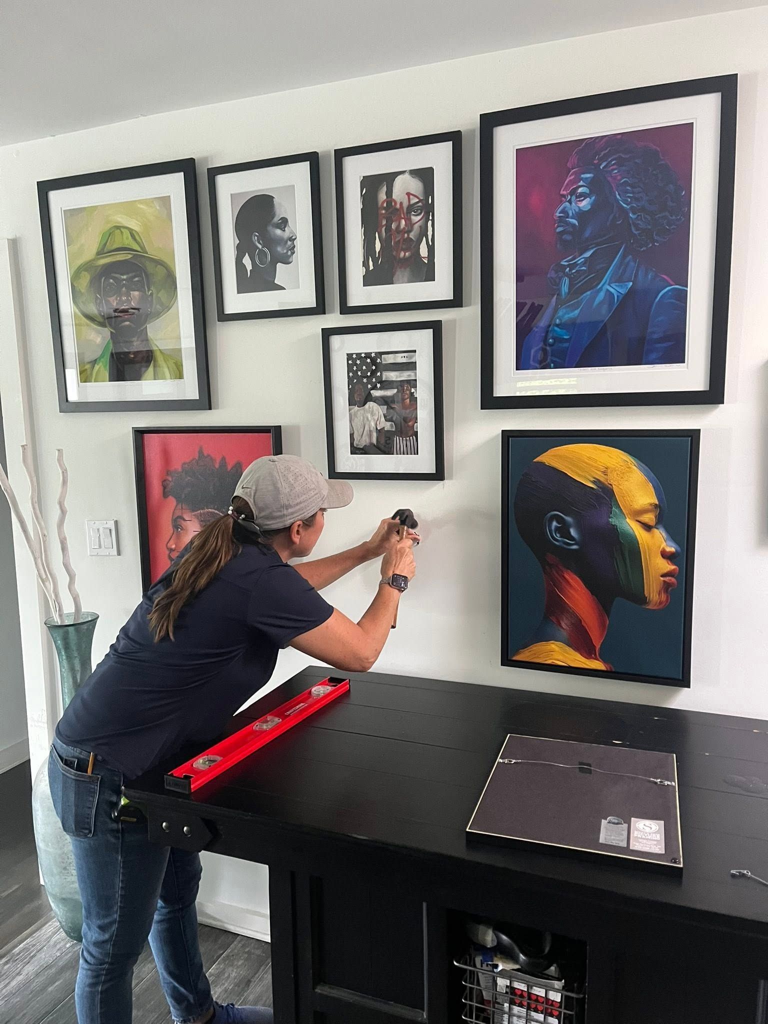 Person hanging framed artwork on a white wall above a black console table
